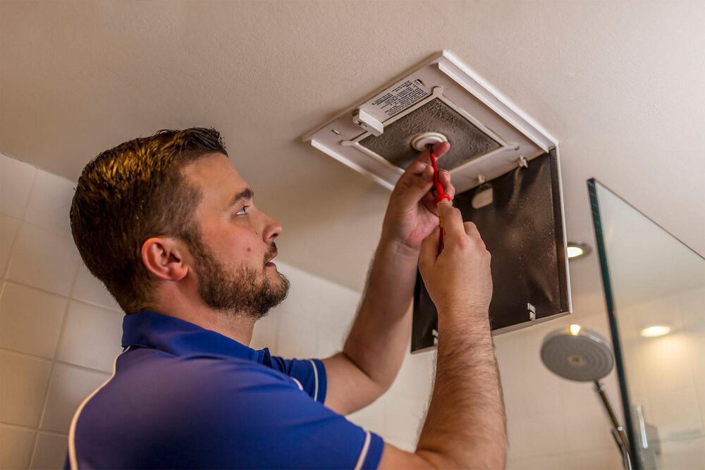 Technician installing bathroom extractor fan – ventilation upgrade and remedial works in London properties